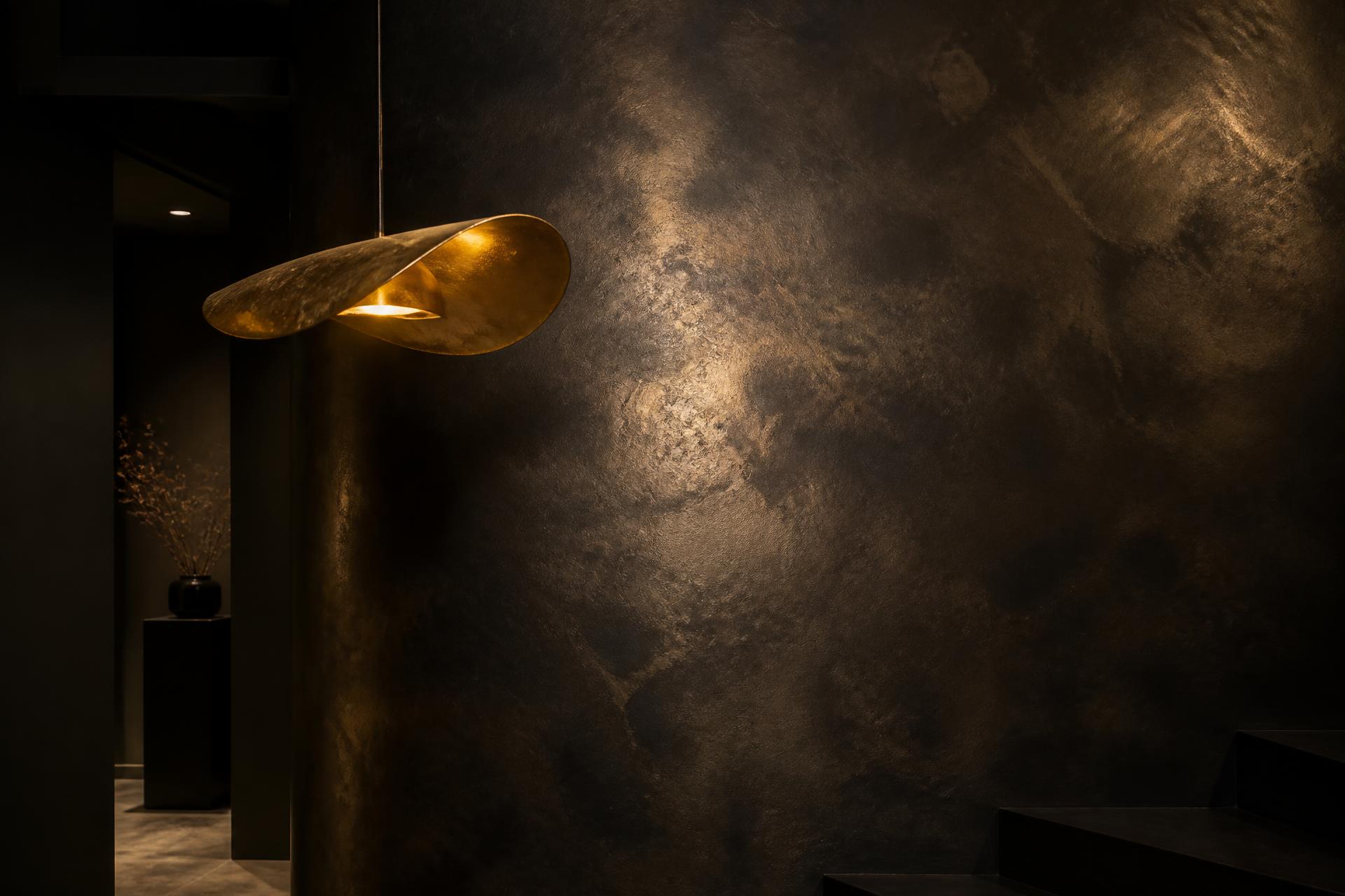 Atmospheric plaster wall lit by a gold pendant