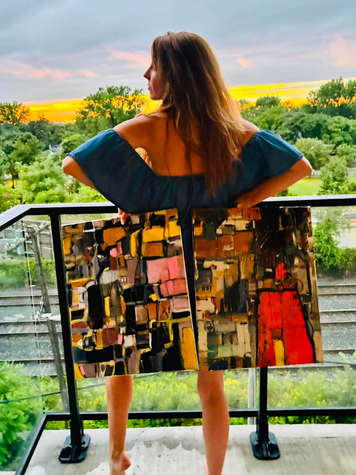 Janet London on a balcony holding one of her abstract paintings